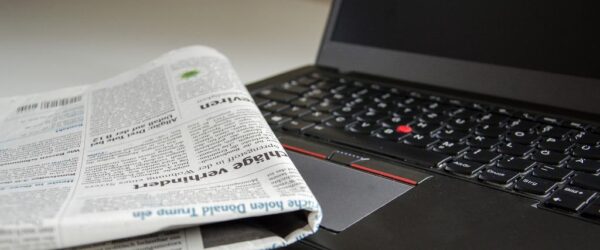 donate-old-computer An old laptop with a newspaper laying on top of it.