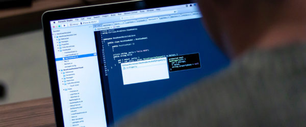 An over-the-shoulder image of a man looking at a laptop screen