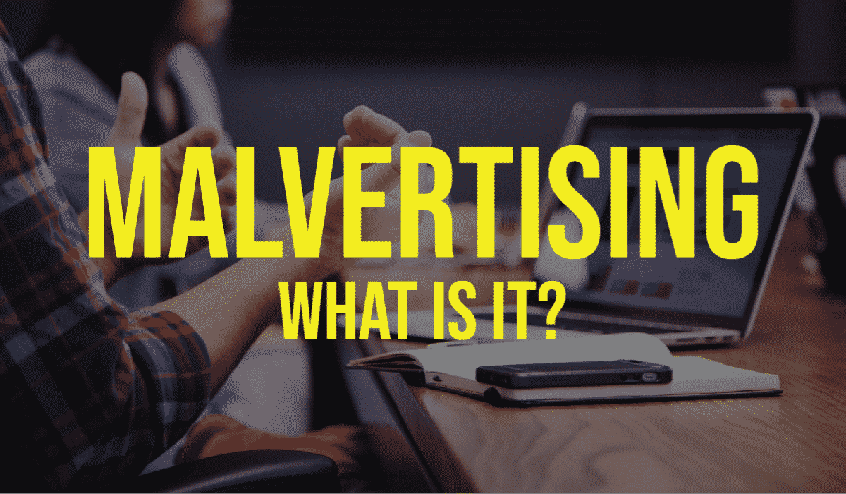 Malvertising – What Is It? Banner - Featuring a person at a table with a computer and laptop on it