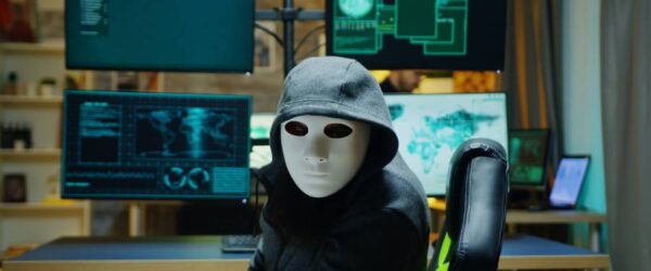 Cybersecurity-Threats-and-Trends-for-2025-What-You-Need-to-Know A hacker attempting to bypass Wilmington cybersecurity while in mask at a multi-monitor setup.