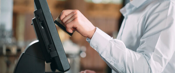 A server wearing a white dress shirt is swiping a card at a POS terminal in a restaurant environment.