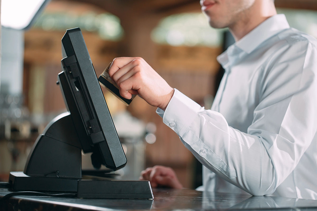A server wearing a white dress shirt is swiping a card at a POS terminal in a restaurant environment.