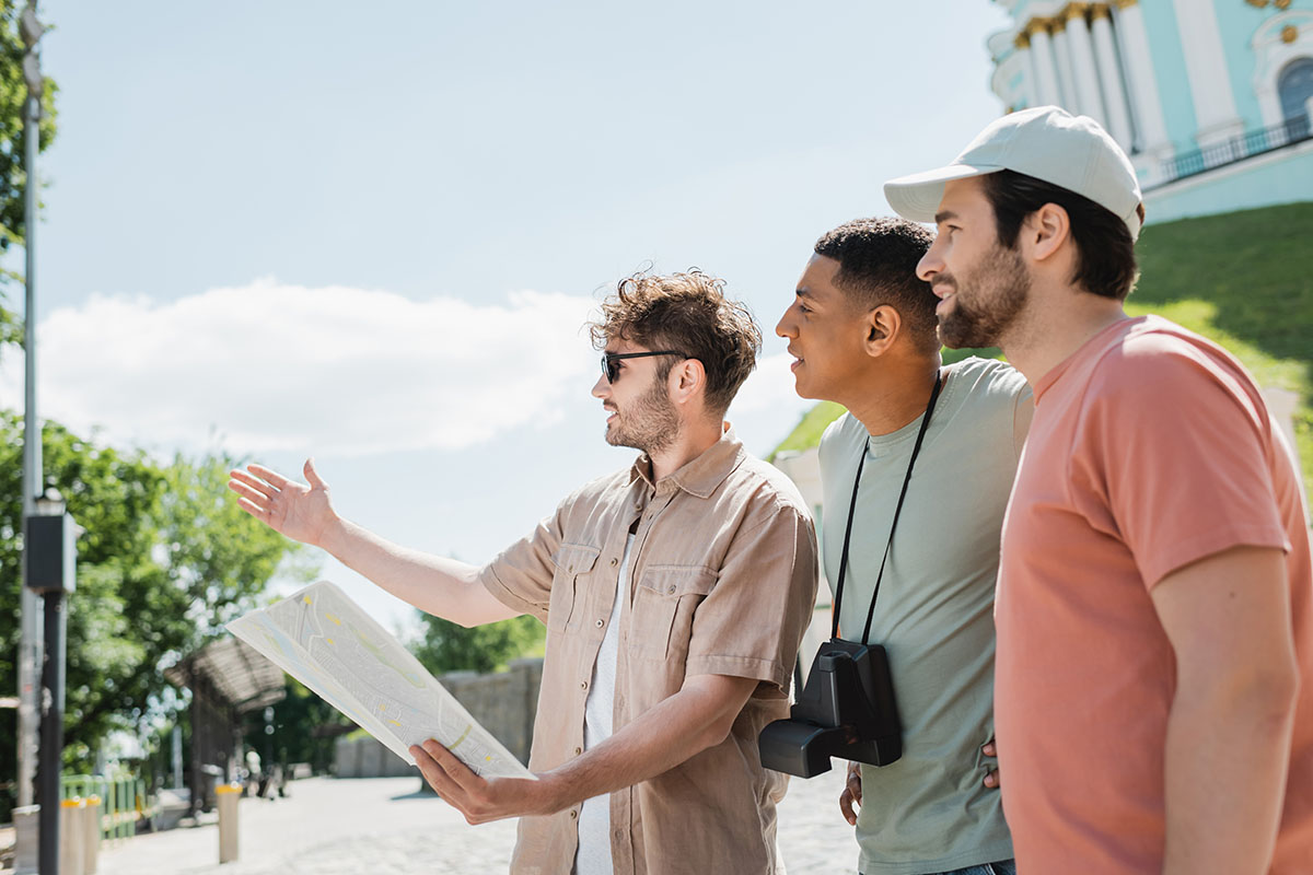 A young tour guide with a city map is pointing with his hand near multicultural travelers on vacation.