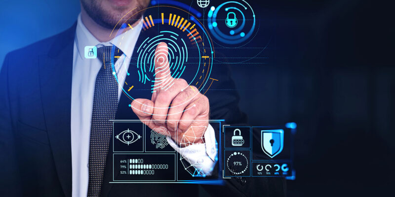 A businessman in a suit is interacting with a futuristic digital interface that displays biometric data and security icons, including a fingerprint, padlocks, and various statistics.