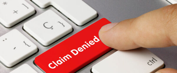 A close-up of a computer keyboard featuring a large red key labelled "Claim Denied," with a finger pressing down on it.