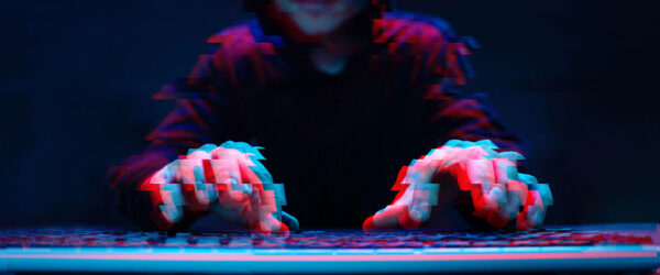 A hooded figure sits in front of a keyboard in a dark setting, with hands hovering over the keys, creating an abstract, glitch-like effect in vibrant blue and red tones.