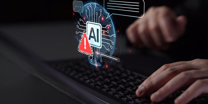 A person typing on a laptop with a digital graphic glowing above the keyboard showing an AI microchip icon next to a red warning sign.