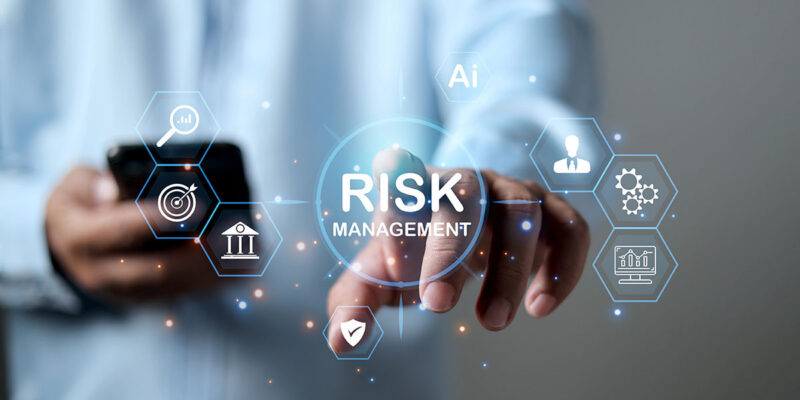 A person reaching out to tap a floating digital icon that reads "RISK MANAGEMENT" surrounded by business and technology symbols.