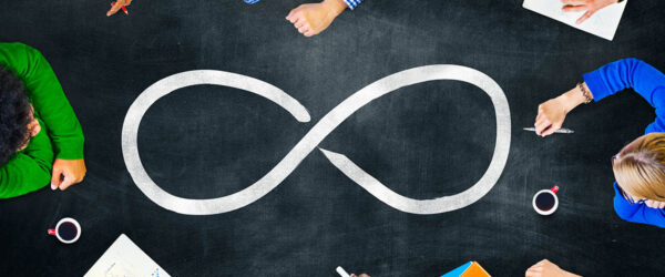 Top-down view of a team sitting around a dark table with a large drawn infinity symbol in the center.