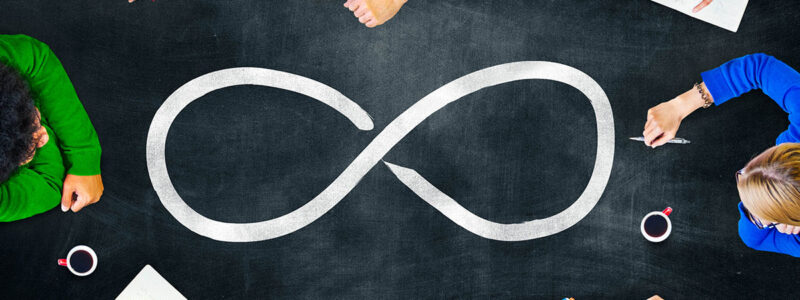Top-down view of a team sitting around a dark table with a large drawn infinity symbol in the center.